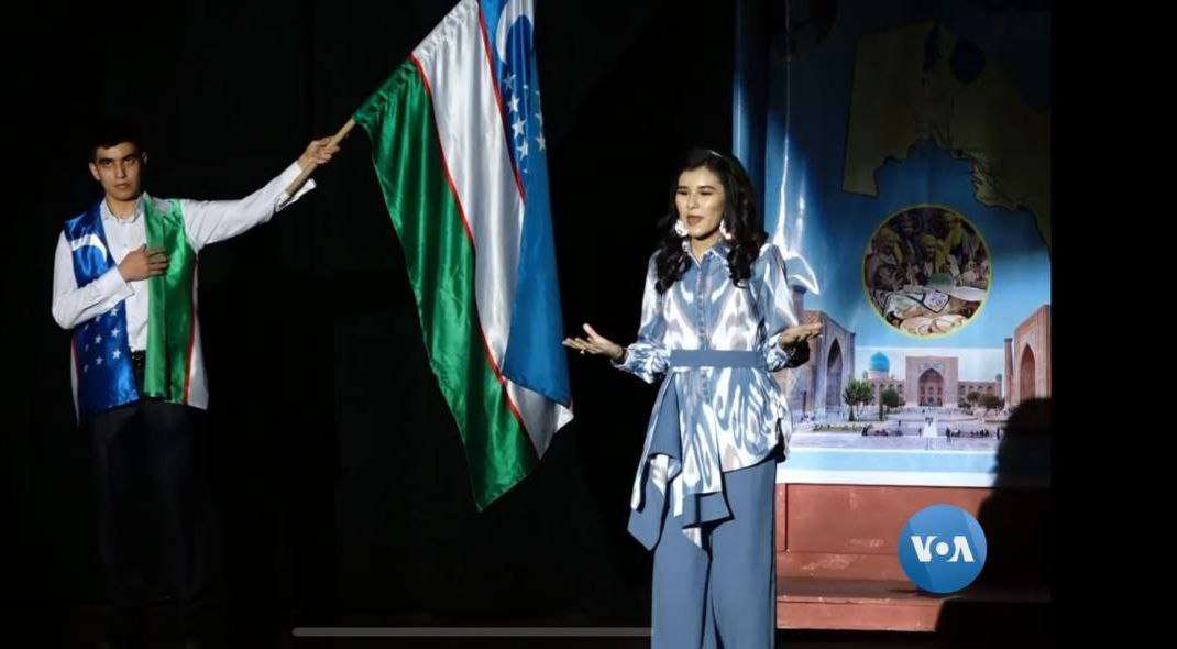 Performers waving the flag of Uzbekistan during a stage production