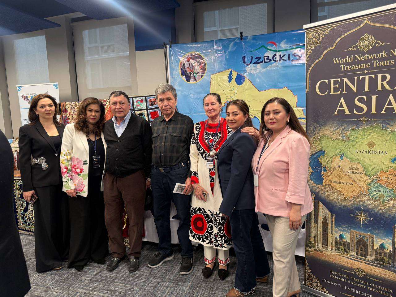 Guests in traditional dress beside a Central Asia banner at a cultural showcase