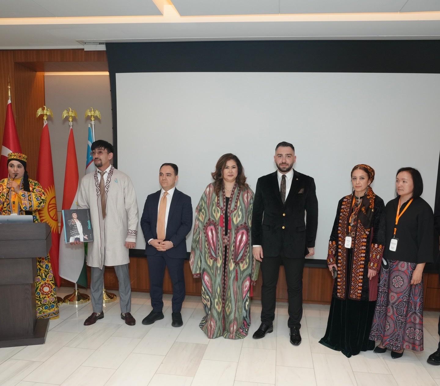 Speakers and guests in traditional and formal dress lined up on stage before the flags of Turkic nations at a Navruz reception