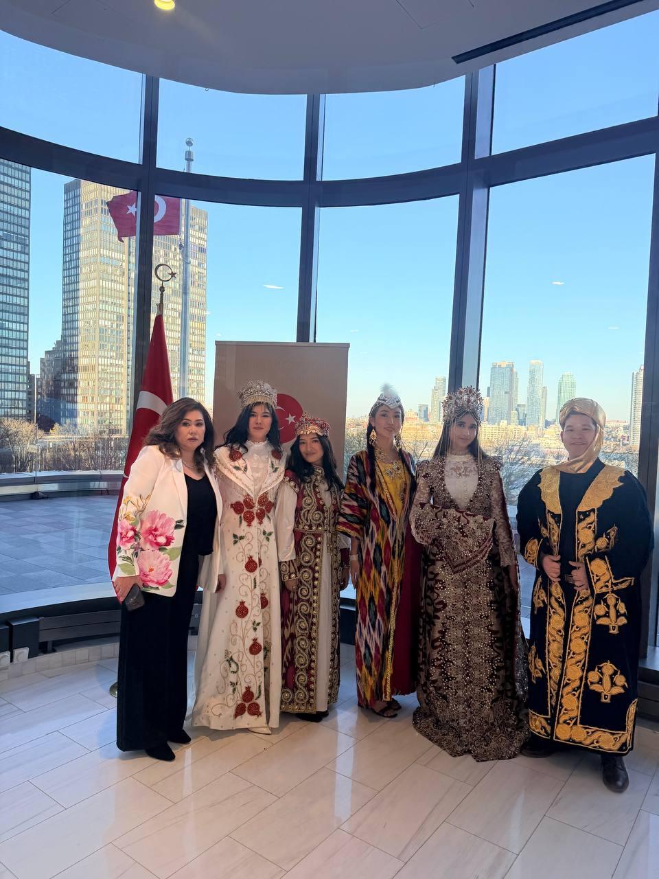 Women in embroidered traditional gowns and crowns before floor-to-ceiling windows overlooking the Manhattan skyline